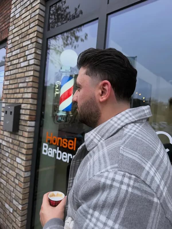 Klant met koffie voor de gevel van Honsel Barbers in Honselersdijk